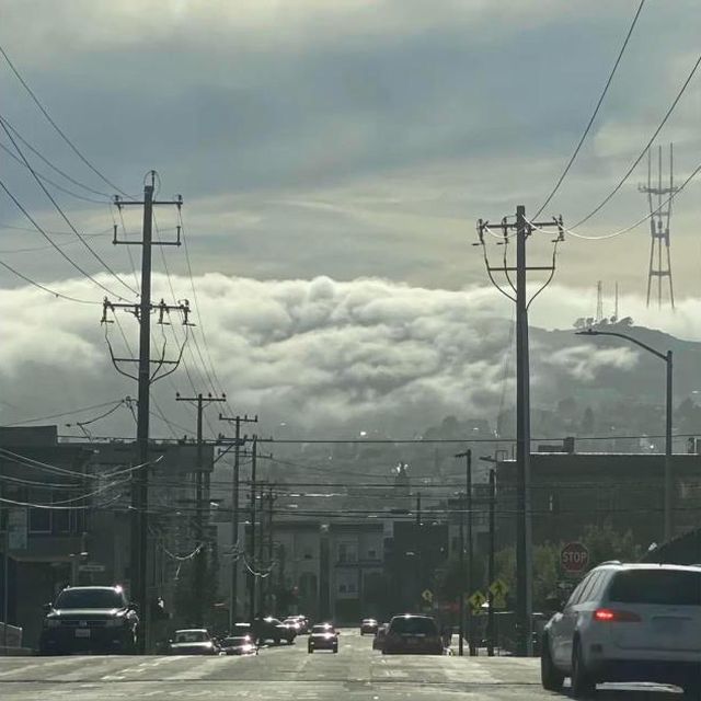 Fog pouring over the ridge at the end of a long street lined with power poles