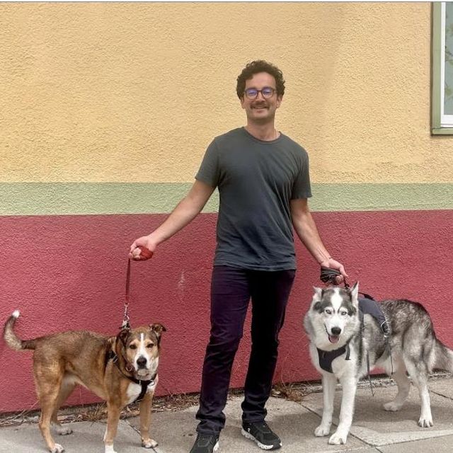 Daniel on the sidewalk with two dogs on leash in front of a painted wall